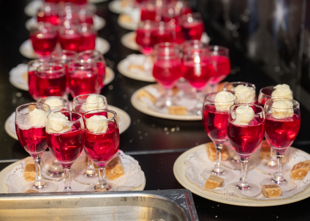 Red jelly desserts with cream topping on a buffet table.