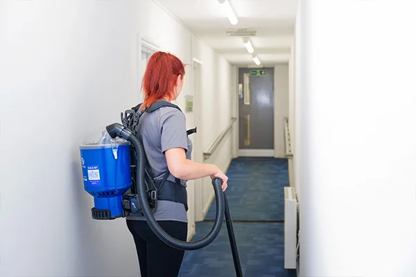 Woman using backpack vacuum cleaner to deep clean an office corridor in Scotland.