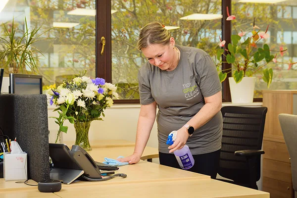 Woman sanitizing office desk with spray cleaner.