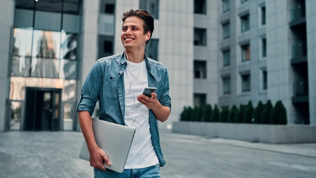 Smiling man with laptop and phone outdoors.